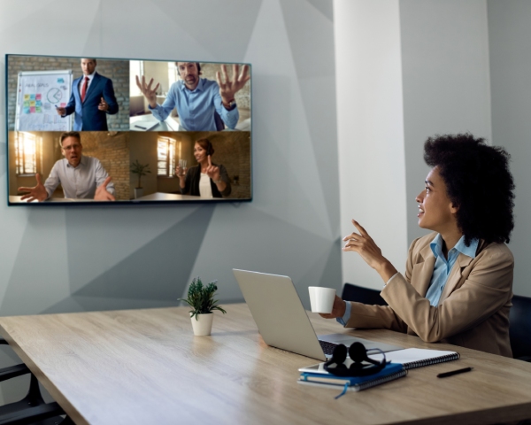 Black businesswoman talking to coworkers via projection screen during video call in the office.